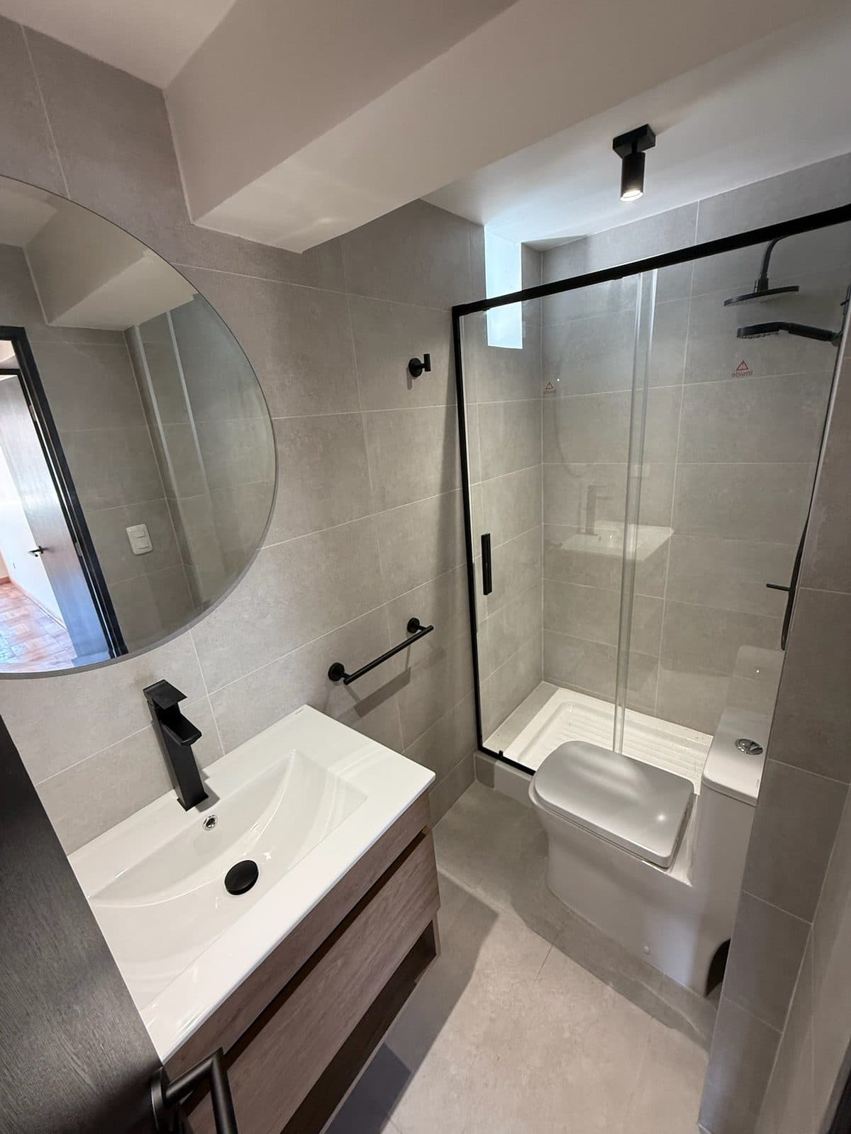 Baño con espejo redondo y vanitorio de madera